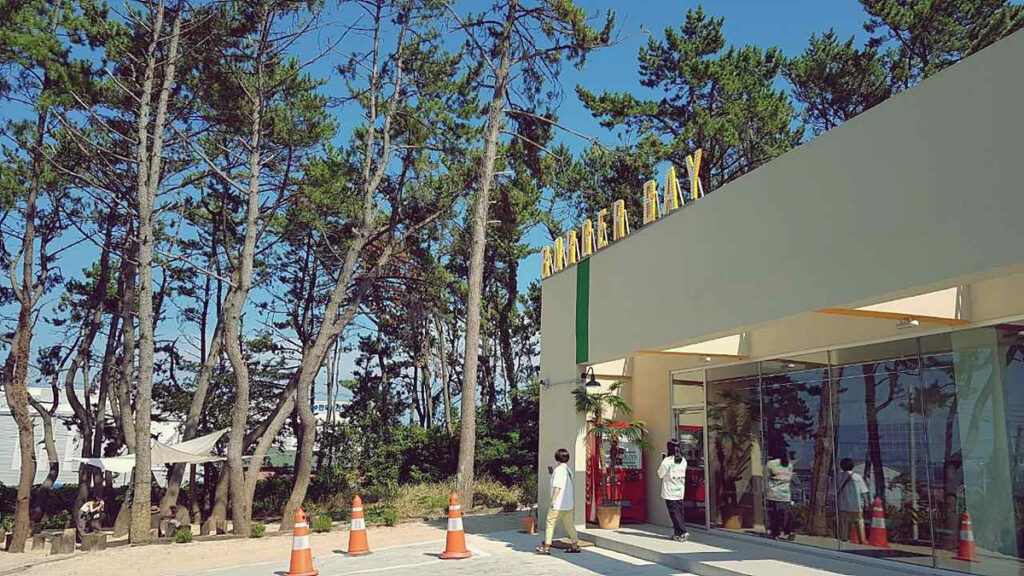 Exterior of Burger Bay in Gijang, surrounded by tall pine trees on a sunny day.
