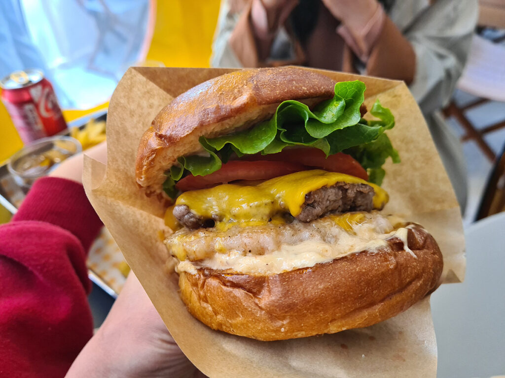 Close-up of the Golden Bay Burger with beef patty, shrimp patty, cheese, lettuce, and tomato.