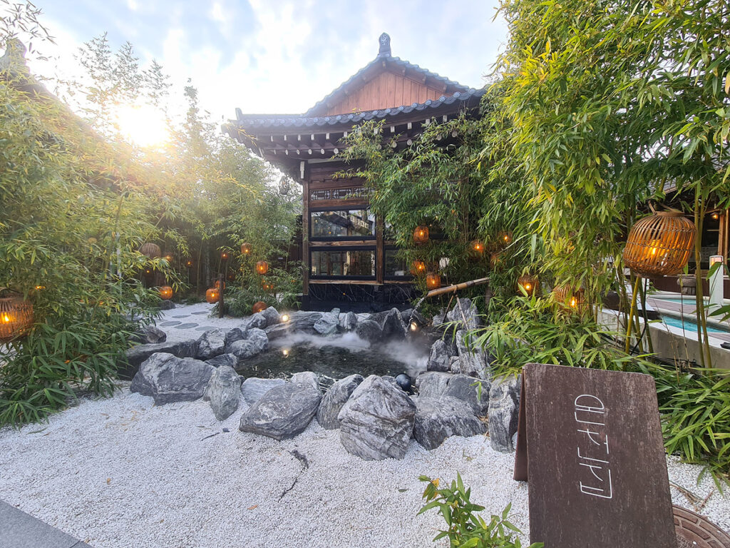 Front view of Oncheonjib’s hanok-inspired exterior, surrounded by bamboo and lanterns, with a peaceful pond at the entrance.